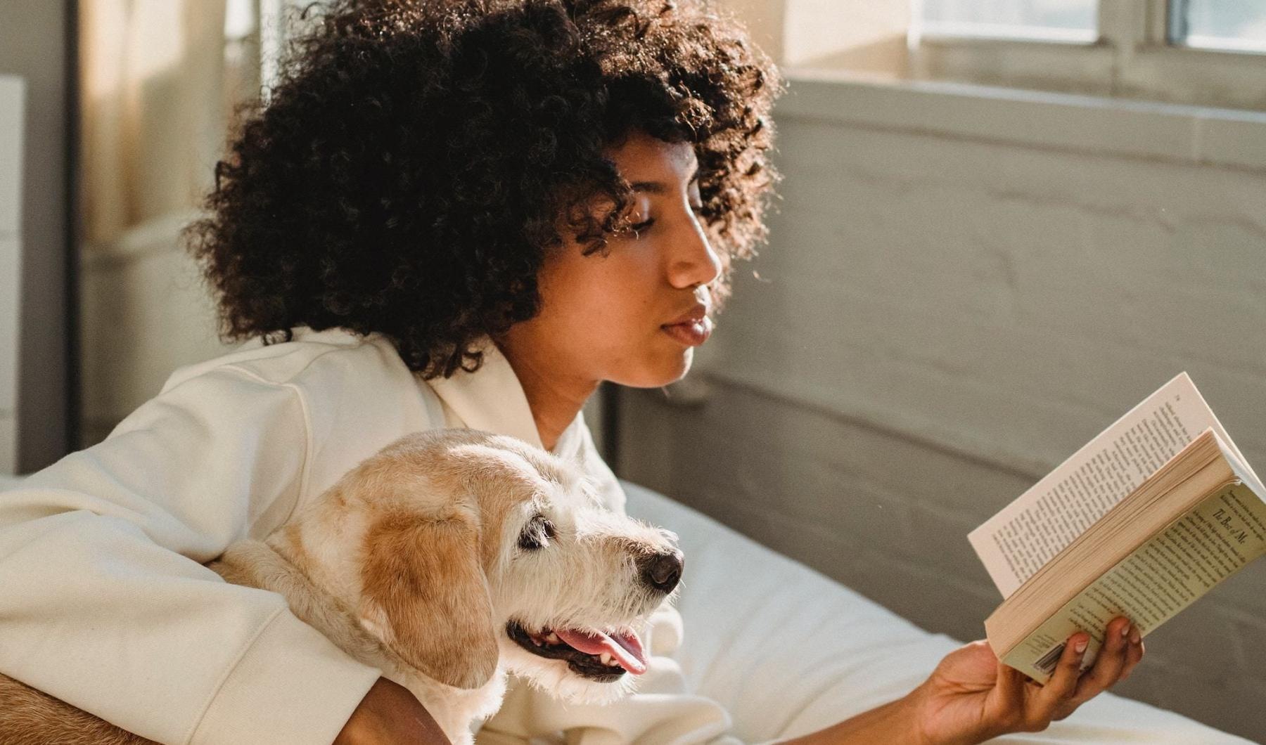 a person reading a book while laying next to a dog