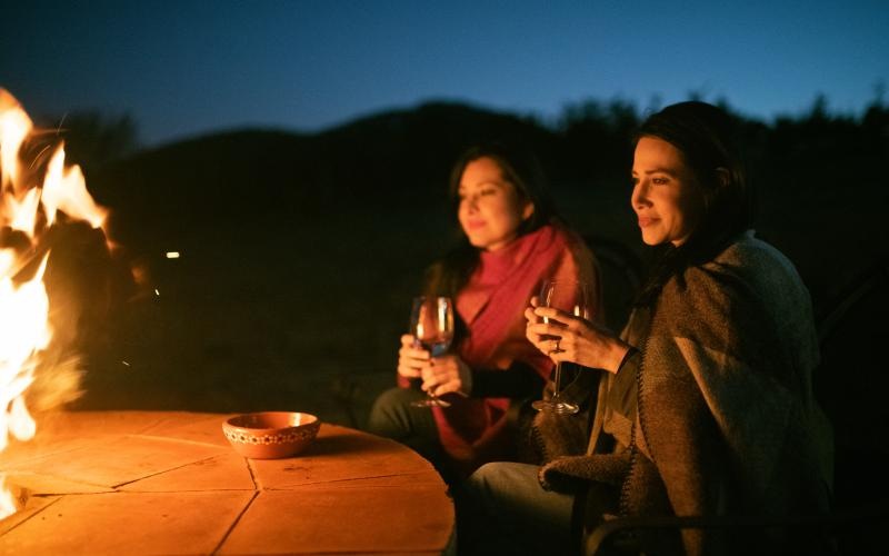 a couple of women sitting at a table with a fire in the background