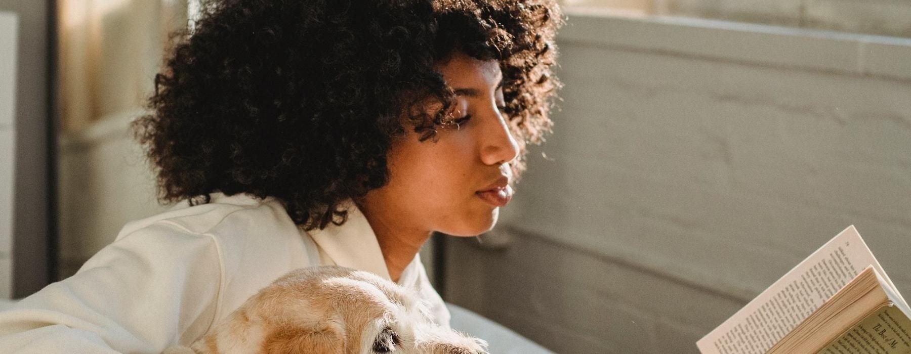 a person reading a book while laying next to a dog